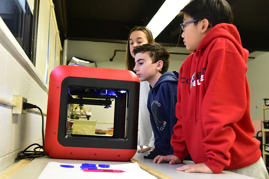 Three students observing a 3D printer